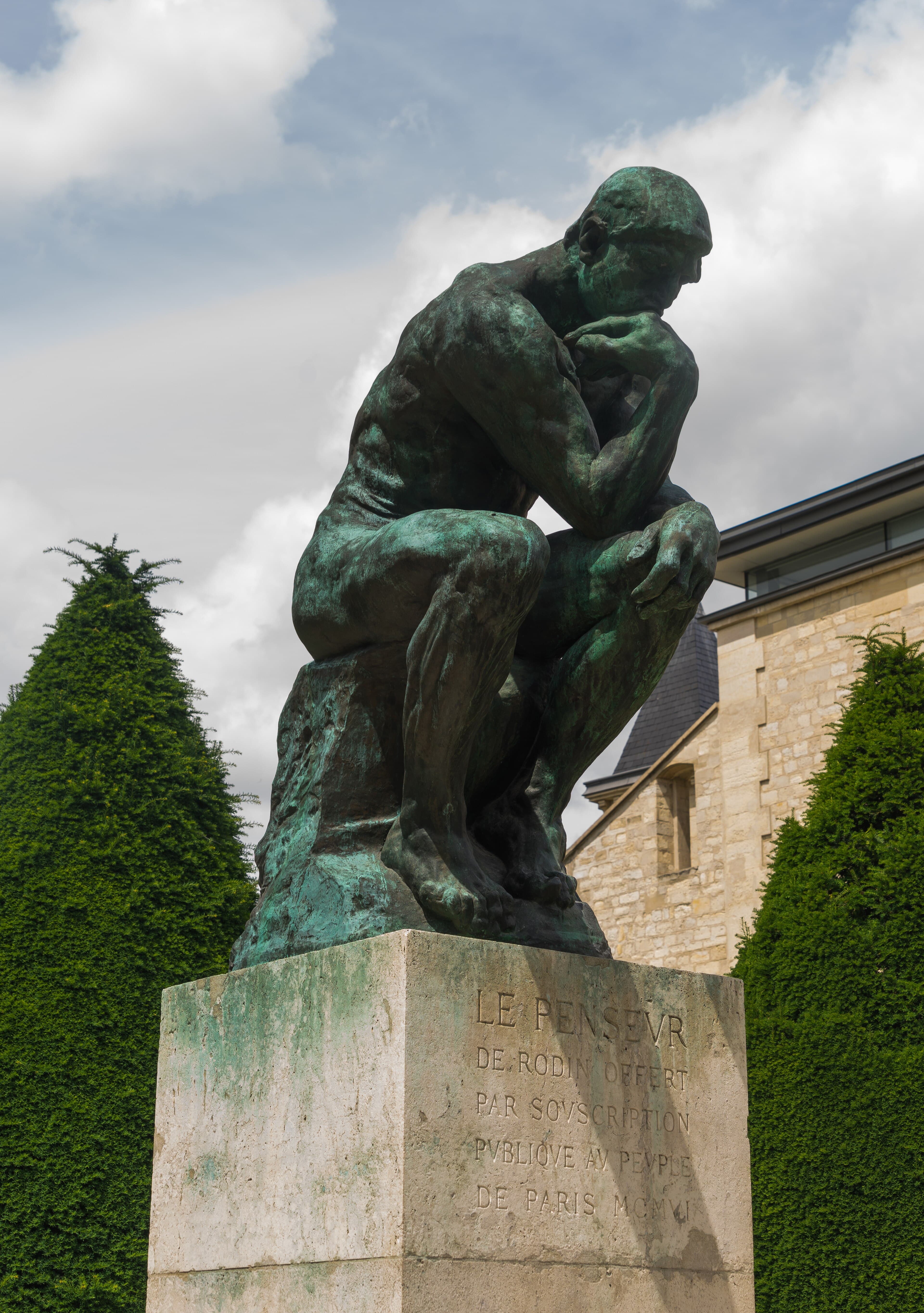 A green-patinated bronze of a nude man seated on a rock, chin resting on his hand, on a stone pedestal in a garden — Auguste Rodin, The Thinker, monumental cast of 1904, Musée Rodin, Paris